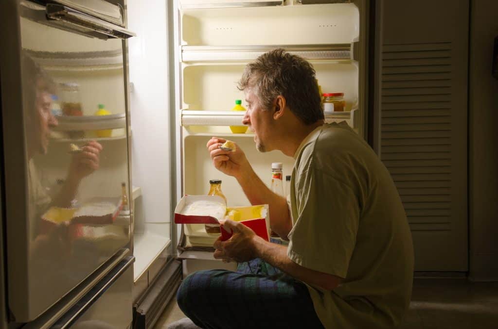 man eating in front of the fridge