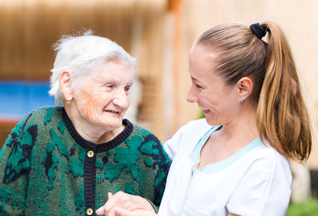 A hospice nurse and the elderly woman she is taking care of smile each other while holding hands